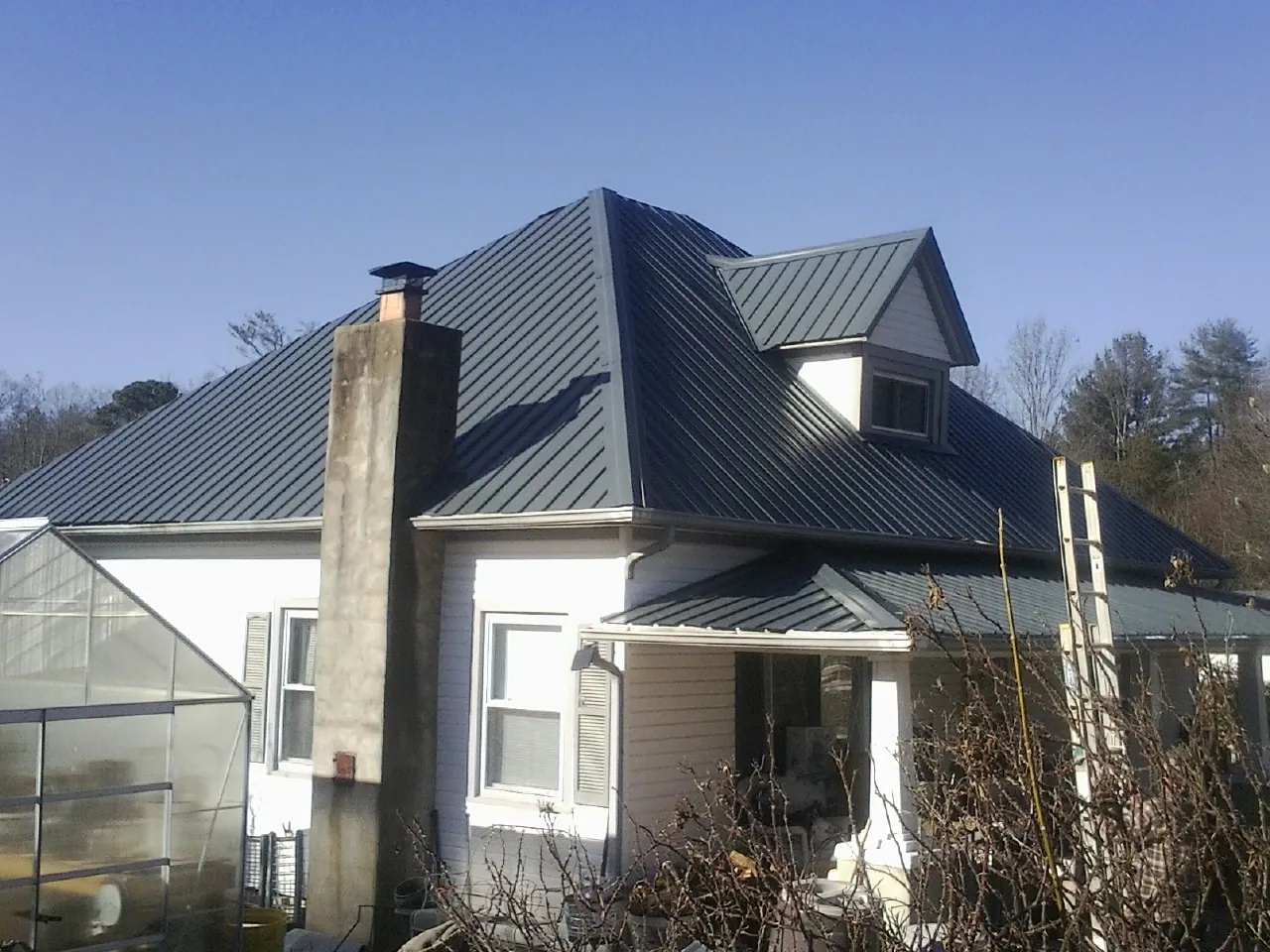 Dark blue standing seam metal roof on a white farmhouse with dormer — Slate & Tile Roof Repair by Roofing Brothers in Wellfleet