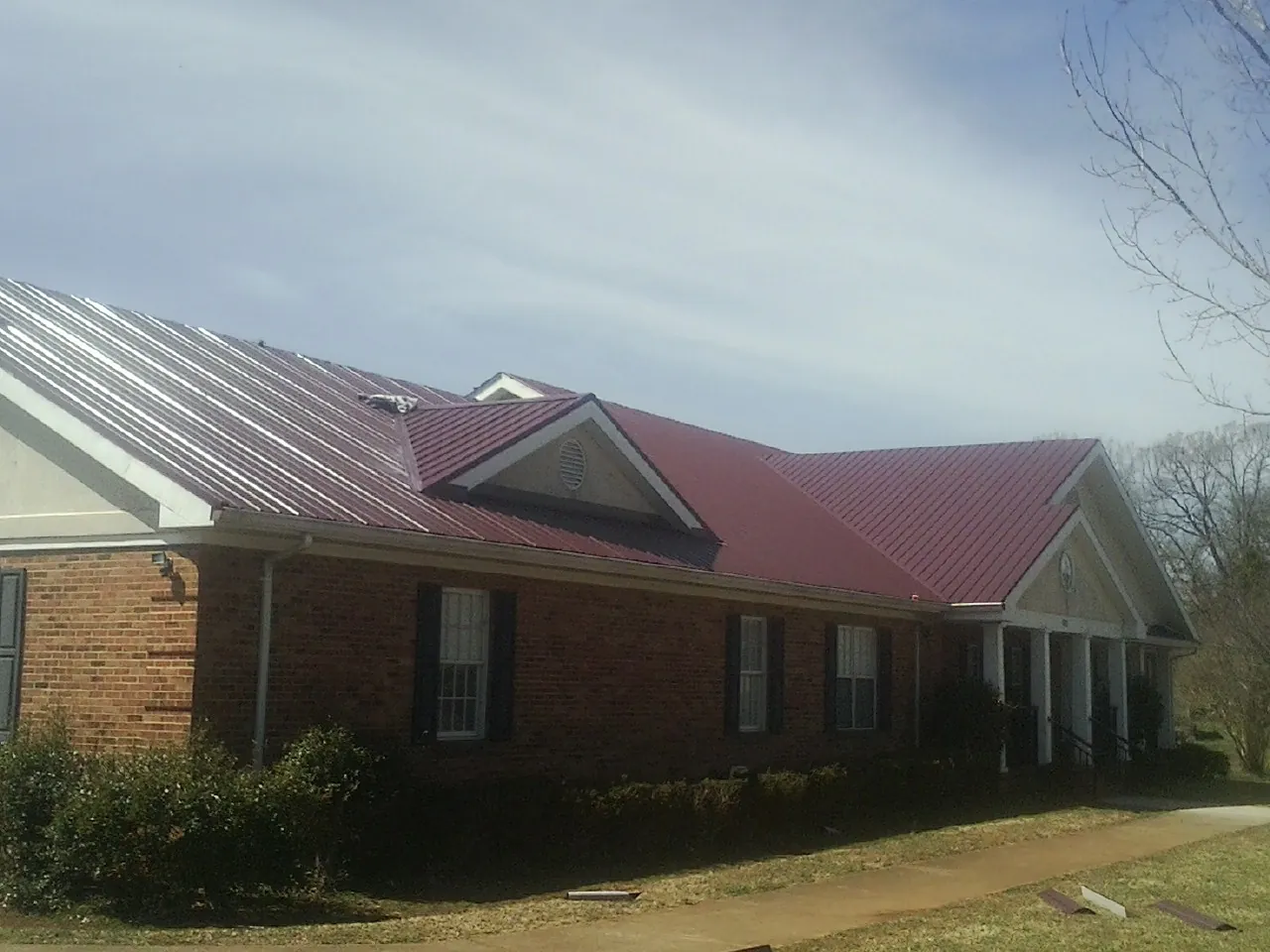 Red metal roof with gabled entries on a long brick building, from a Hail Damage Roof Repair job in Wellfleet