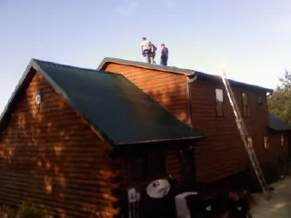 Crew on the ridge of a green metal roof on a two story log home in Wellfleet