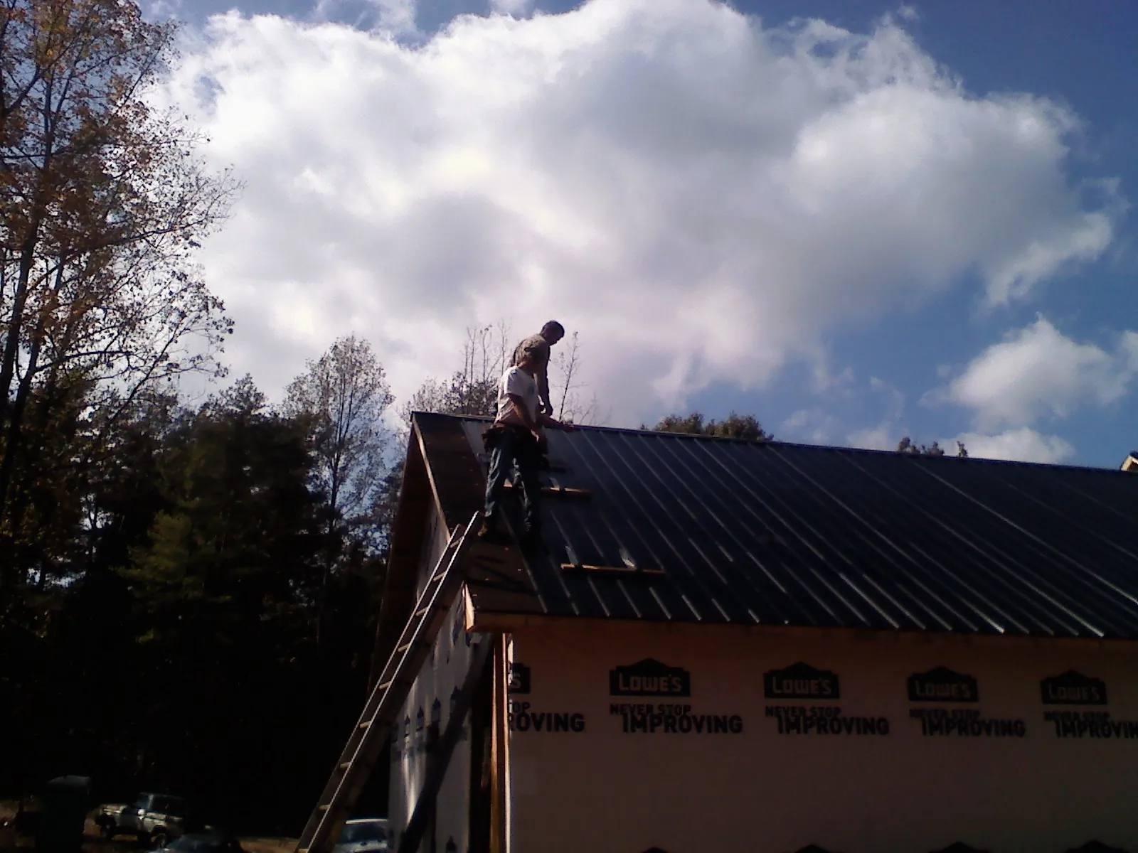 Roofer fastening dark metal panels high against a cloudy sky, from a Roof Inspection job in Wellfleet