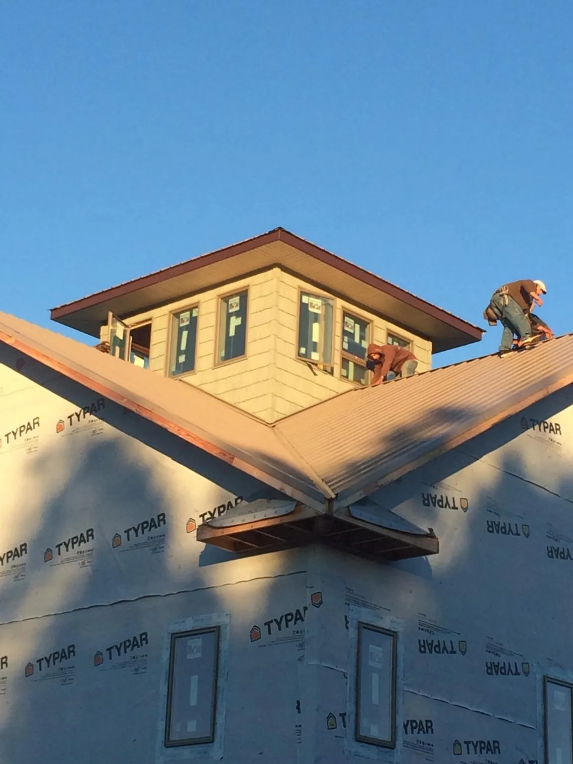 Roofers working around a rooftop cupola on a new metal roof at sunset — Roof Waterproofing in Wellfleet by Roofing Brothers